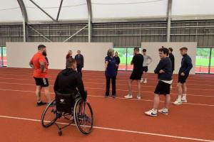 group of students on an indoor athletics track receiving disability inclusion training